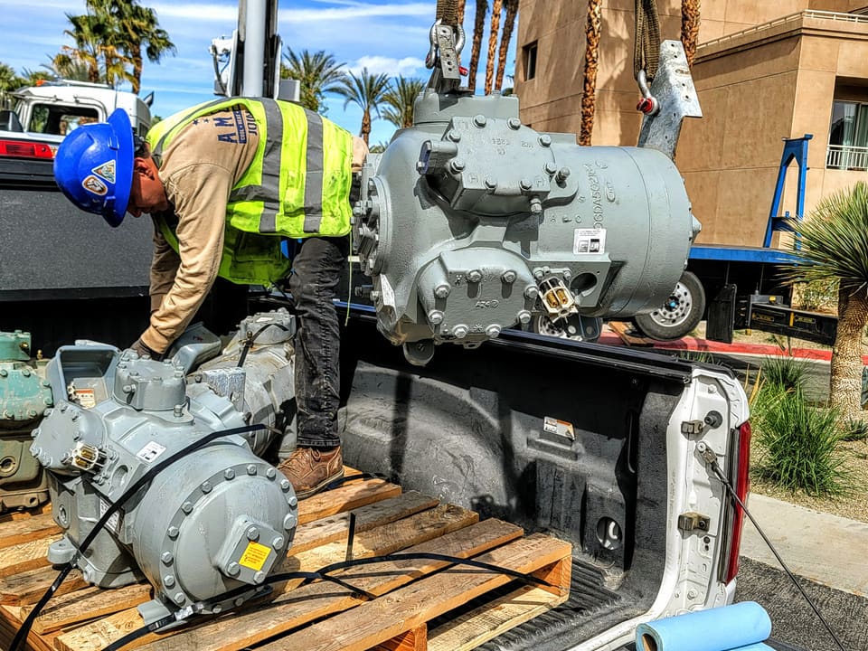 American Cool technician handling large commercial HVAC compressors during a repair